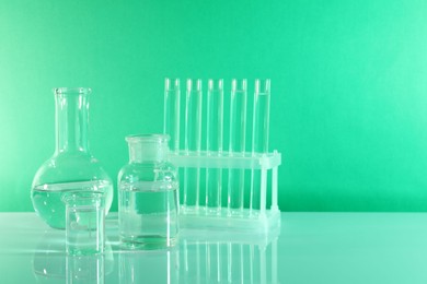 Photo of Laboratory analysis. Different glassware on table against green background, space for text