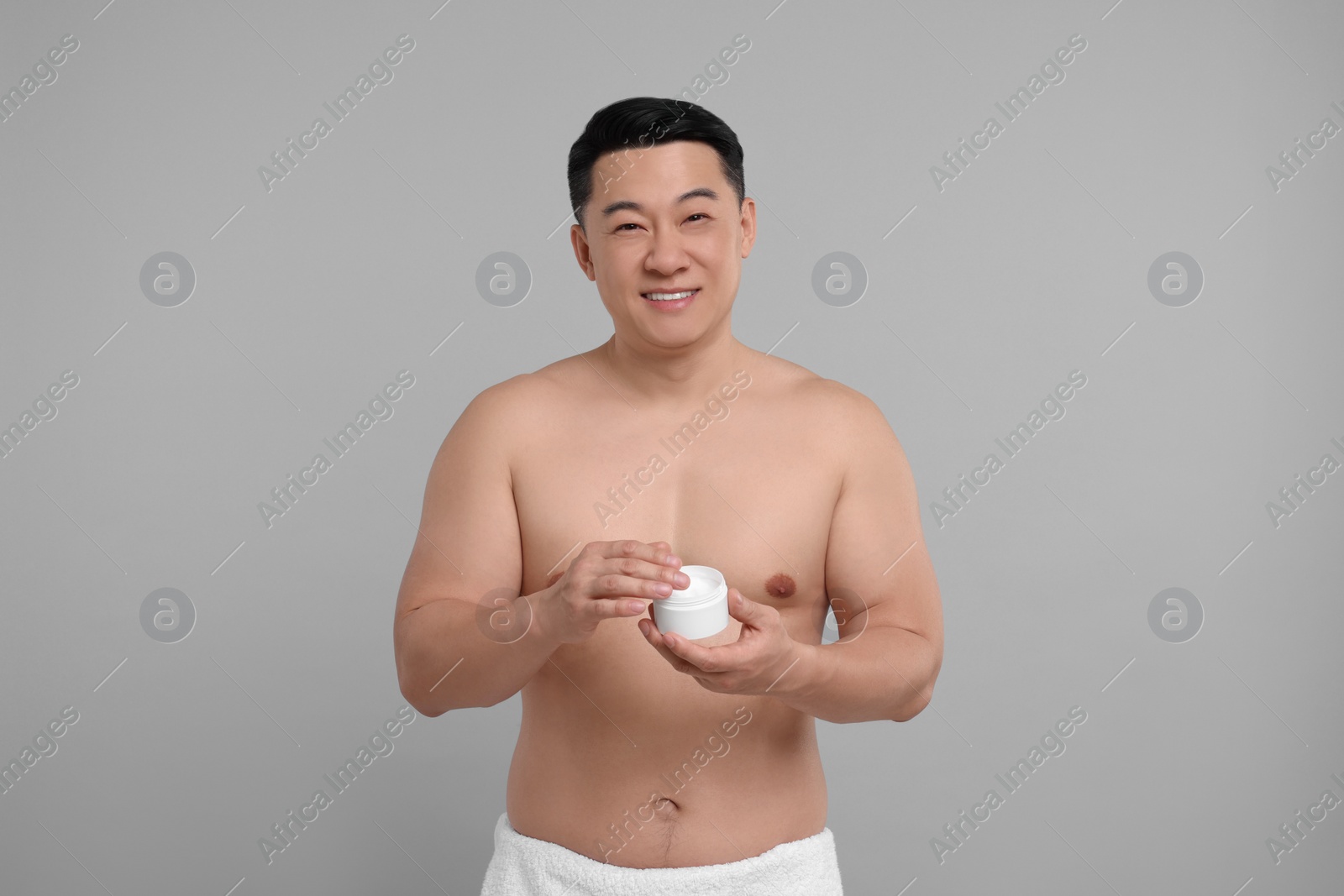 Photo of Handsome man with jar of body cream on light grey background