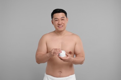 Handsome man with jar of body cream on light grey background