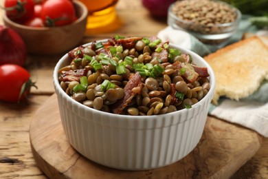 Delicious lentils with bacon and green onion in bowl served on wooden table, closeup