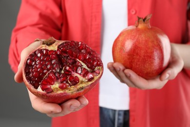 Photo of Woman holding whole and cut pomegranates on grey background, closeup
