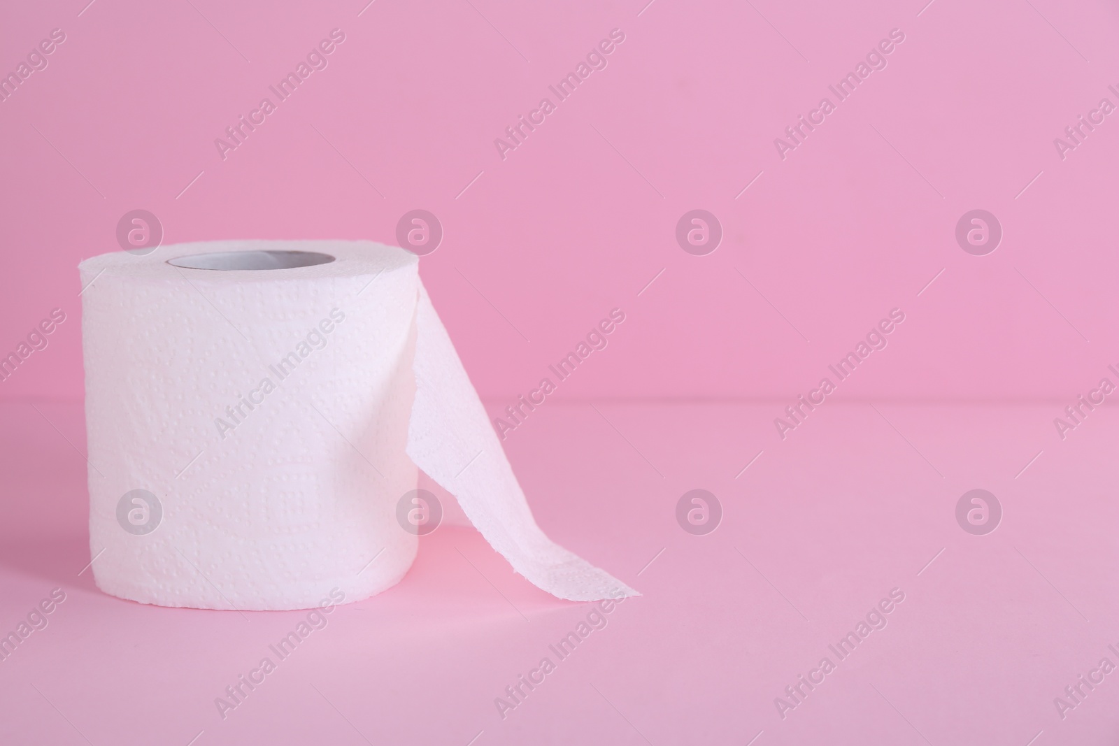 Photo of Soft toilet paper roll on pink background. Space for text