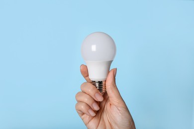 Photo of Woman holding LED light bulb on blue background, closeup