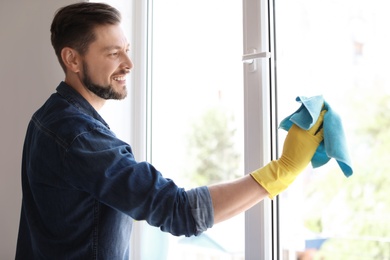 Photo of Man in casual clothes washing window glass at home