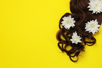 Lock of healthy brown hair with flowers on yellow background, top view. Space for text