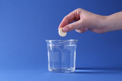 Photo of Woman putting effervescent pill into glass of water on blue background, closeup