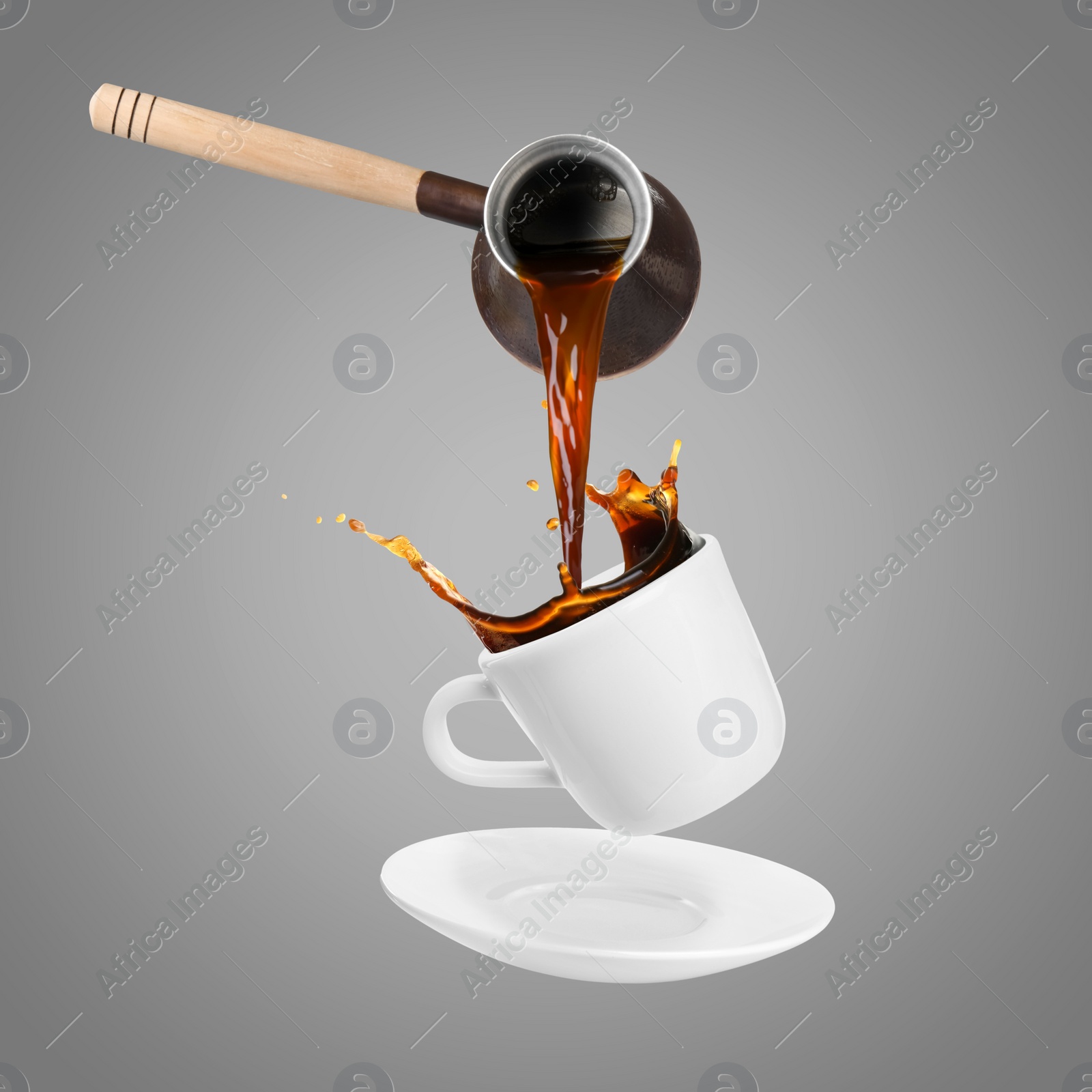 Image of Pouring freshly brewed aromatic coffee from turkish pot into cup. Objects in air on grey background