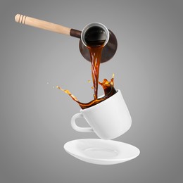 Image of Pouring freshly brewed aromatic coffee from turkish pot into cup. Objects in air on grey background