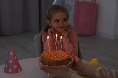 Photo of Birthday celebration. Mother holding tasty cake with burning candles near her daughter indoors