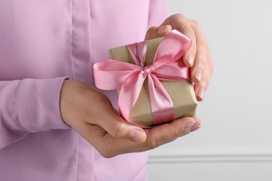Photo of Woman holding gift box with pink bow near white wall, closeup