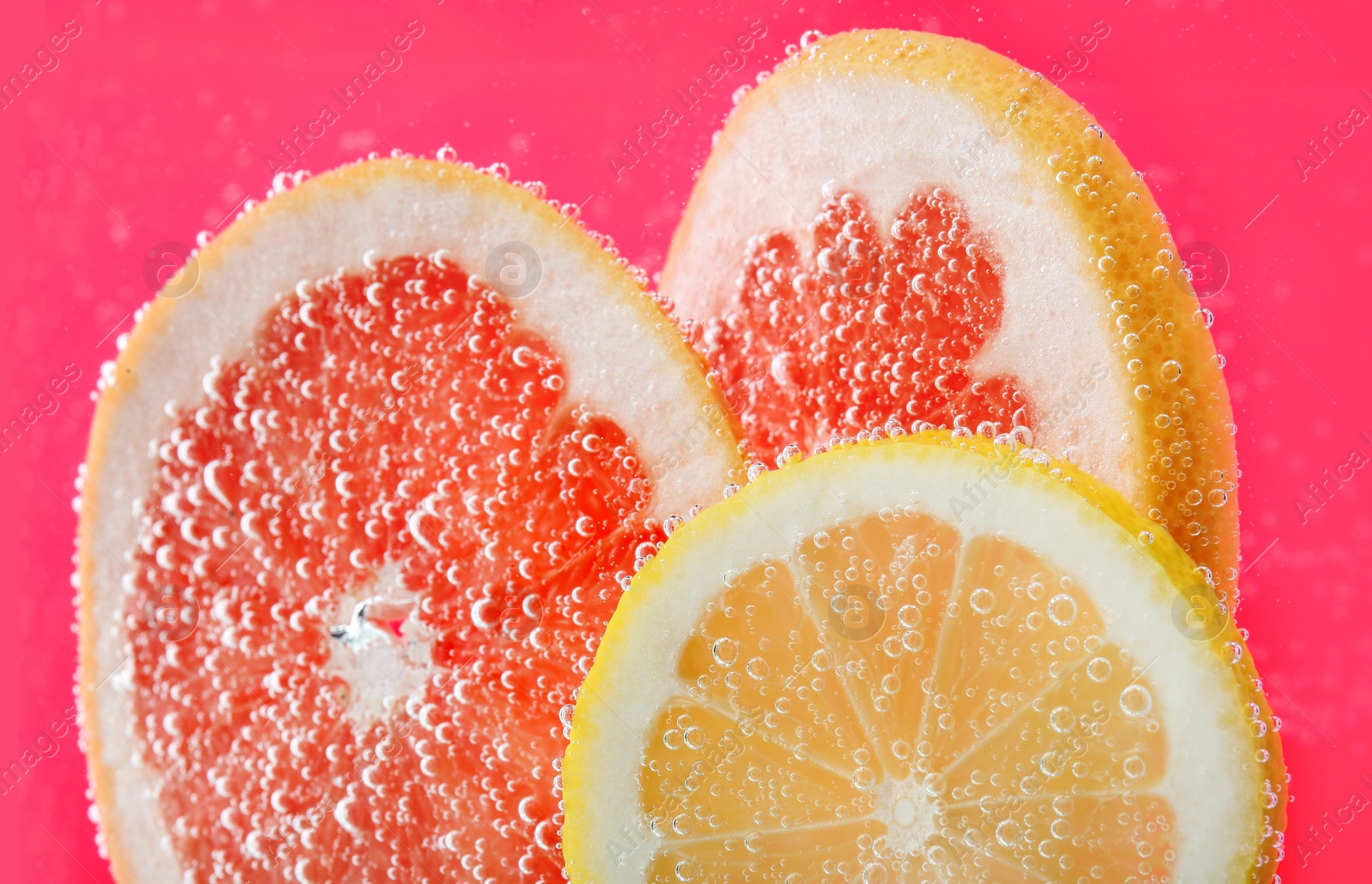 Photo of Slices of different citrus fruits in sparkling water on pink background, closeup