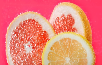 Slices of different citrus fruits in sparkling water on pink background, closeup