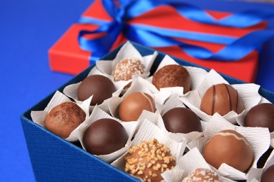 Photo of Box with delicious chocolate candies on blue background, closeup