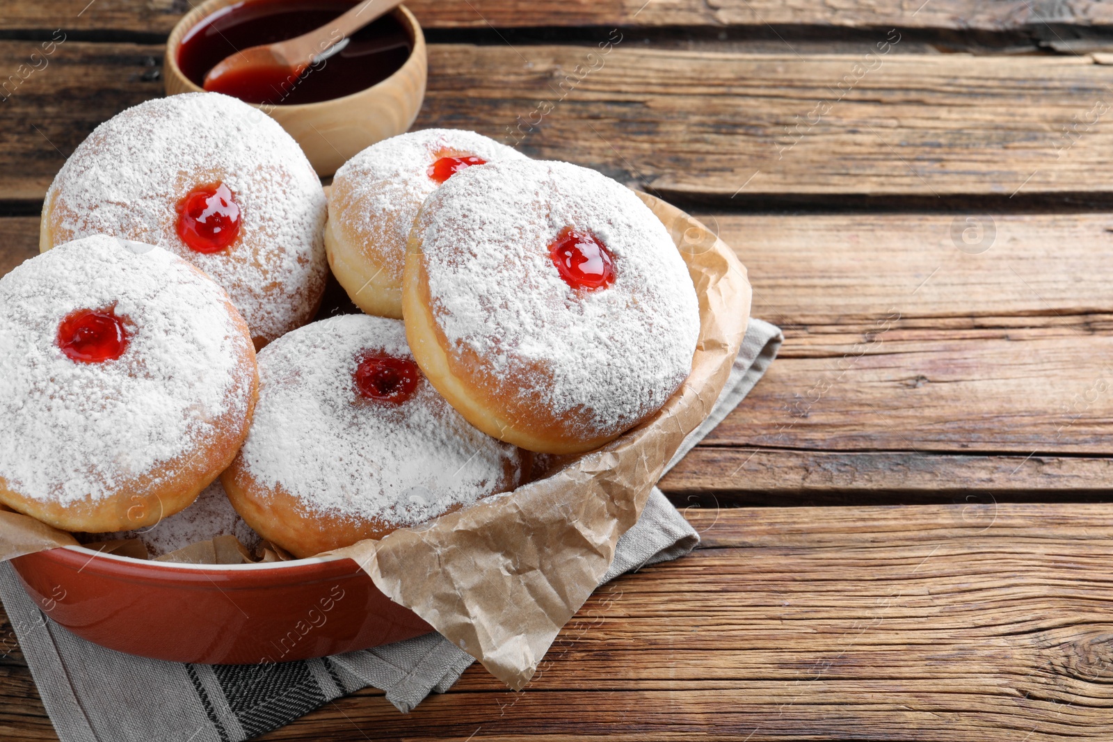 Photo of Delicious donuts with jelly and powdered sugar in baking dish on wooden table. Space for text