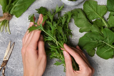 Woman with fresh green herbs at light grey table, top view