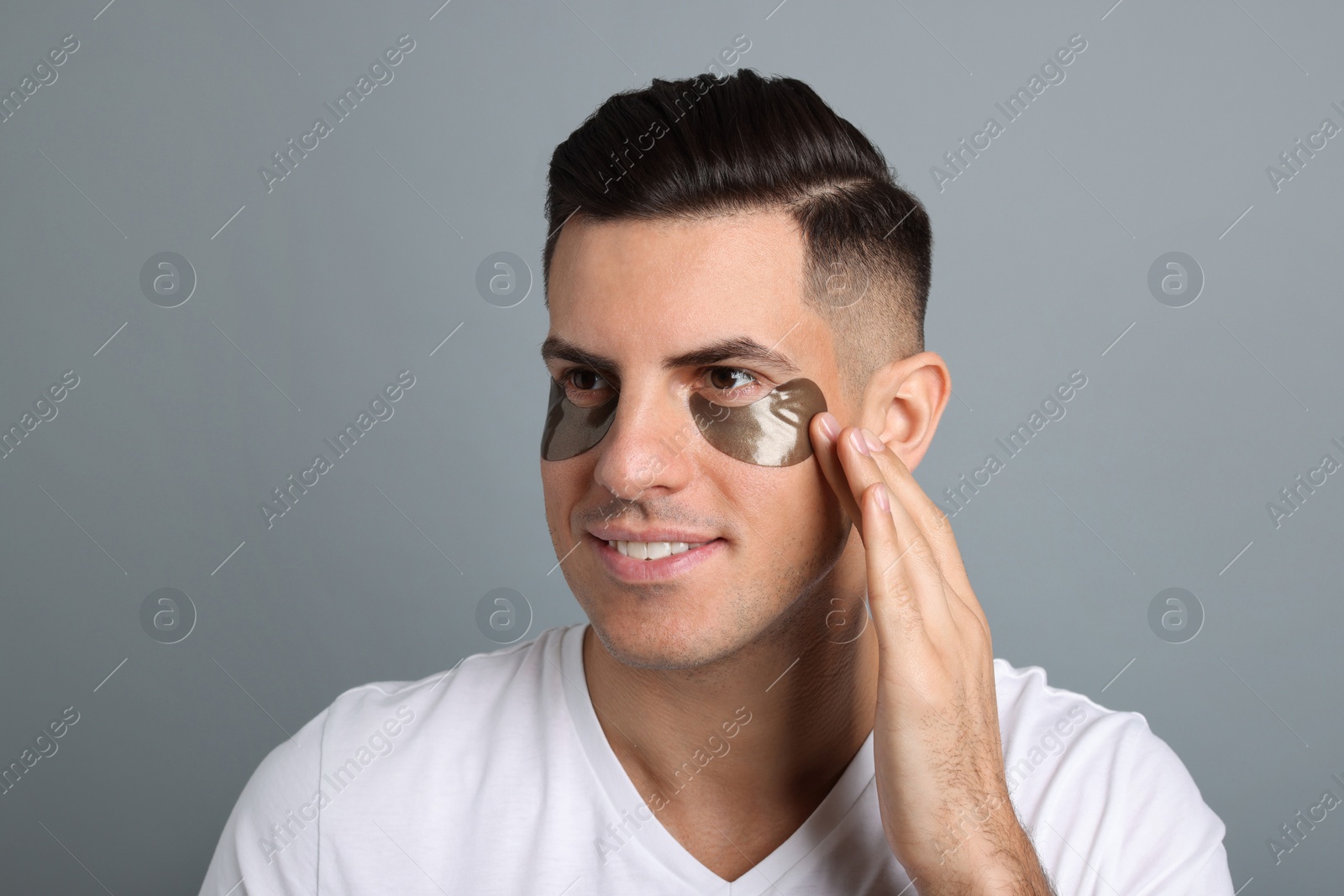 Photo of Man applying dark under eye patch on grey background