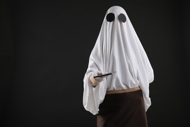 Photo of Creepy ghost. Waiter in white sheet and apron with receipt on black background, space for text
