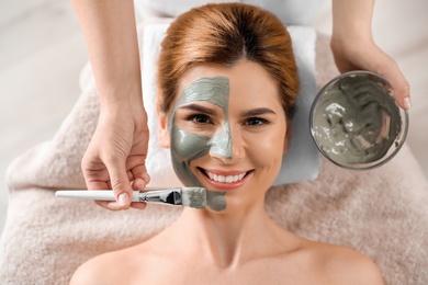 Photo of Cosmetologist applying mask onto woman's face in spa salon, top view