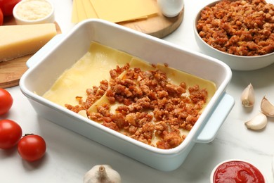 Photo of Cooking lasagna. Pasta sheets, minced meat in baking tray and products on white table, closeup