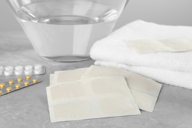 Photo of Mustard plasters, pills, towel and bowl with water on light grey marble table, closeup