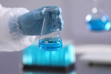 Scientist holding flask with light blue liquid in laboratory, closeup
