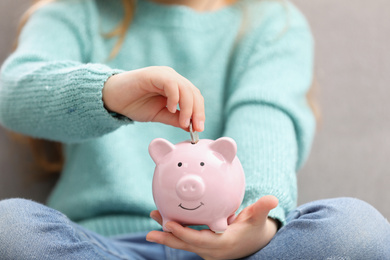 Photo of Girl putting money into piggy bank on light background, closeup