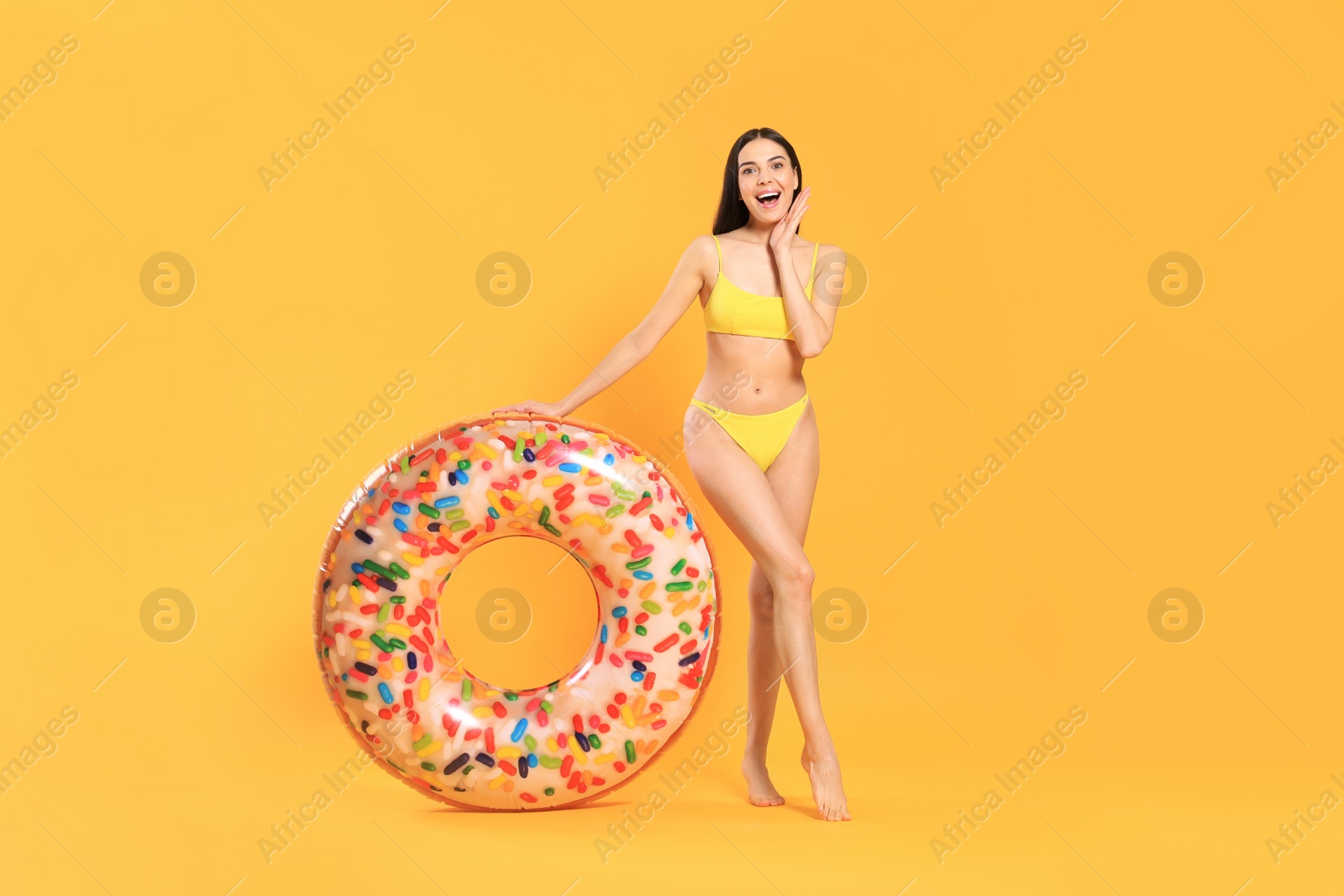 Photo of Happy young woman with beautiful suntan and inflatable ring against orange background