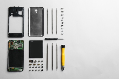 Disassembled mobile phone and repair tools on white background, top view