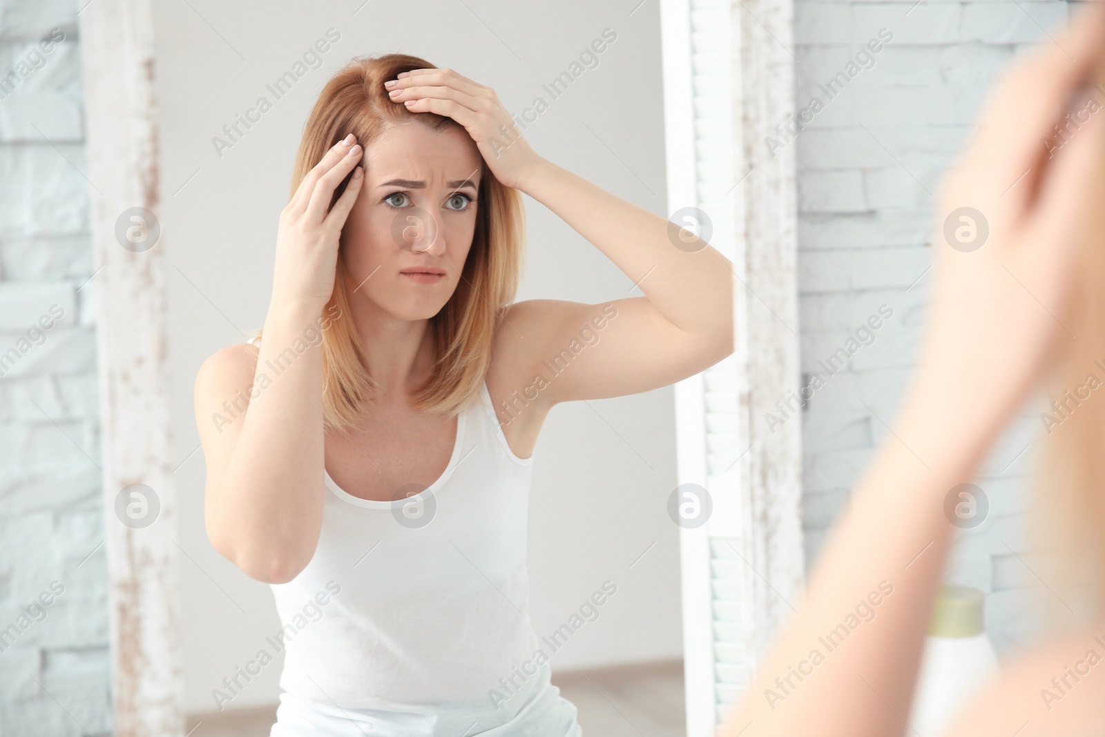 Photo of Young woman with hair loss problem in front of mirror at home