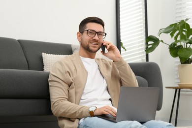 Man talking on smartphone while working with laptop at home