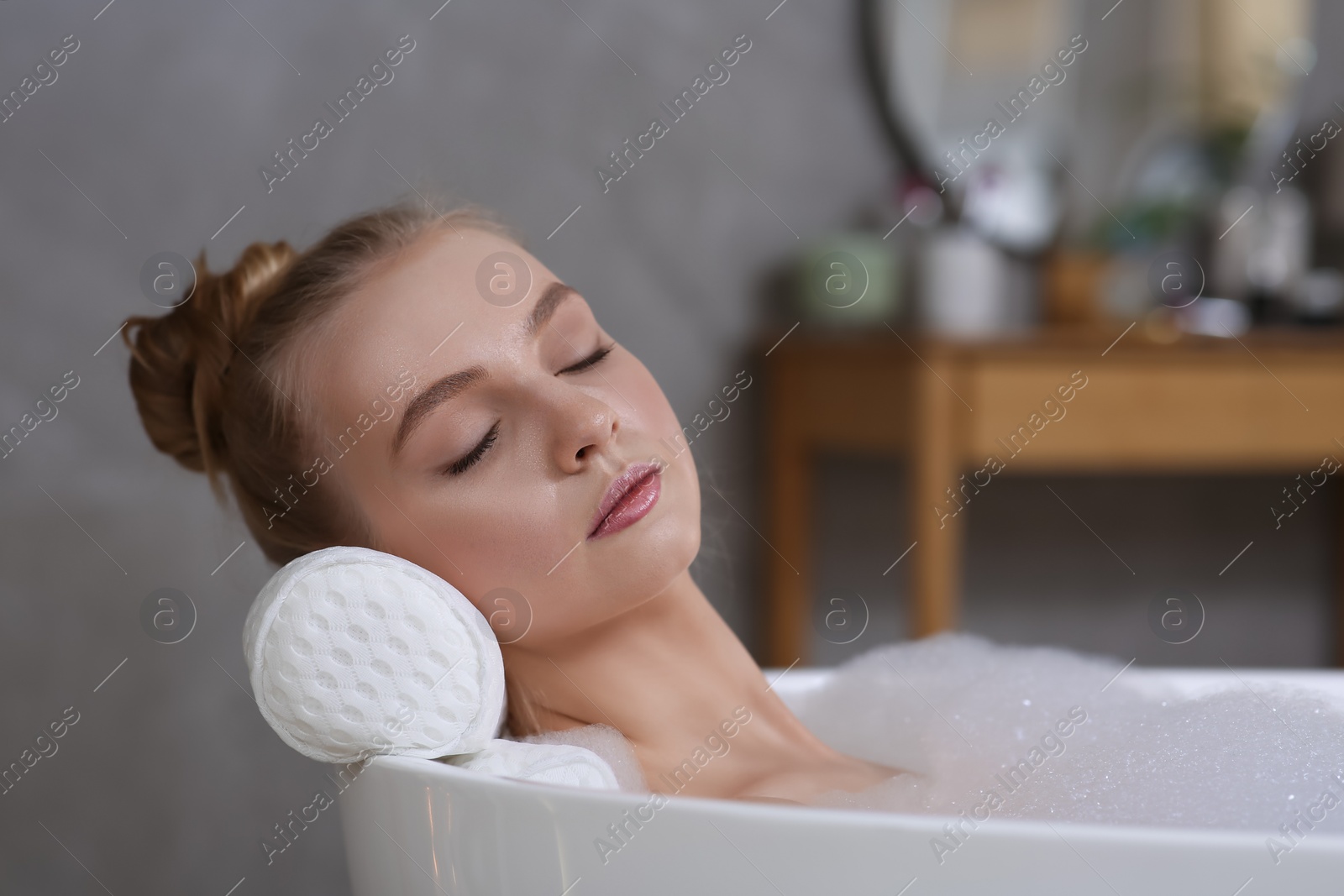 Photo of Young woman using pillow while enjoying bubble bath indoors