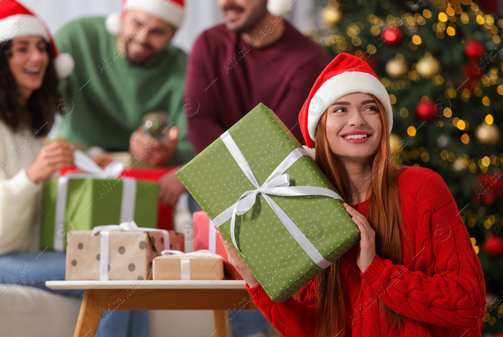 Photo of Christmas celebration in circle of friends. Happy young woman with gift box at home, selective focus