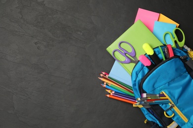 Blue backpack with different school stationery on black stone table, space for text. Back to school