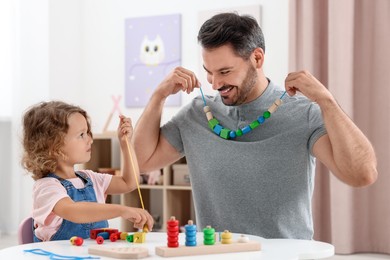 Photo of Motor skills development. Father and daughter playing with wooden pieces and string for threading activity at table indoors