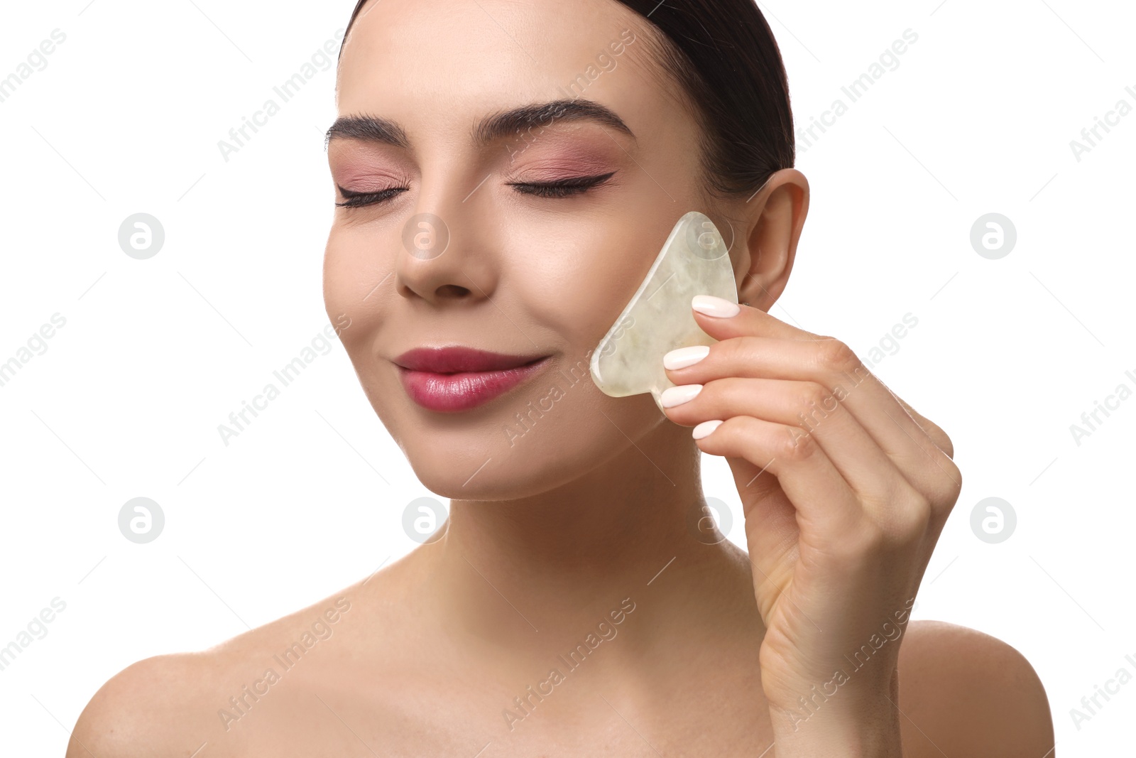 Photo of Beautiful young woman doing facial massage with gua sha tool on white background, closeup