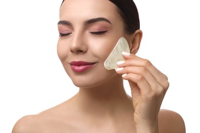 Beautiful young woman doing facial massage with gua sha tool on white background, closeup