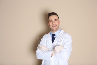 Photo of Male dentist holding professional tools on color background