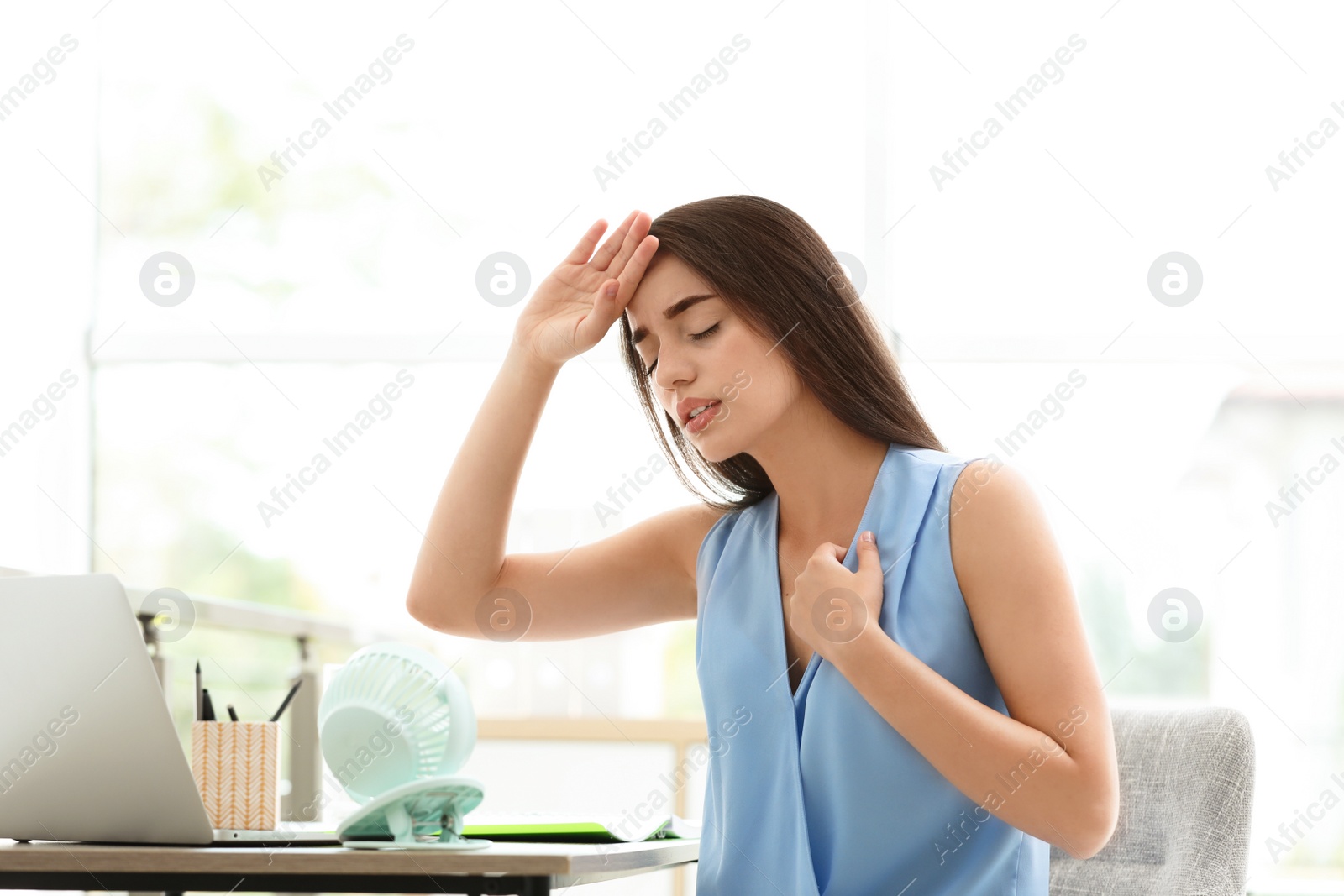 Photo of Woman with portable fan suffering from heat at workplace. Summer season