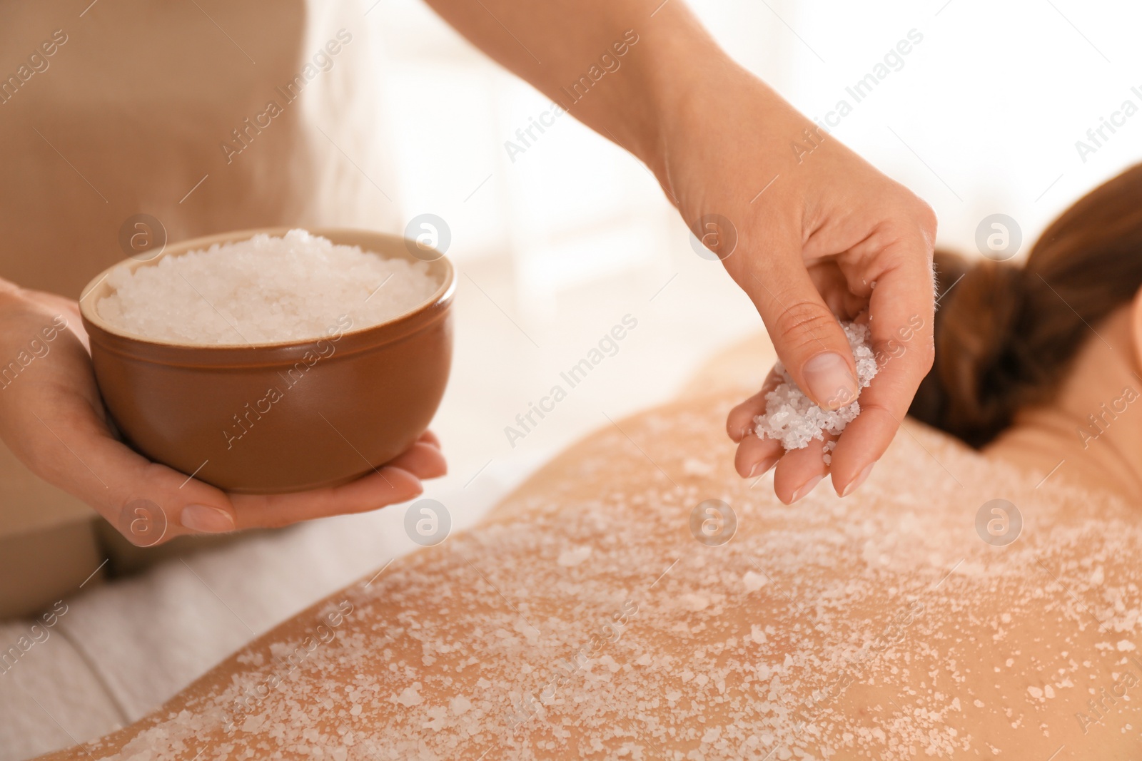 Photo of Young woman having body scrubbing procedure with sea salt in spa salon, closeup