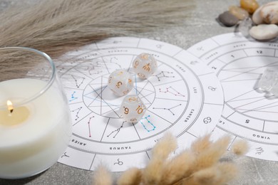 Zodiac wheel, natal chart, burning candle, astrology dices and stones on grey table, closeup