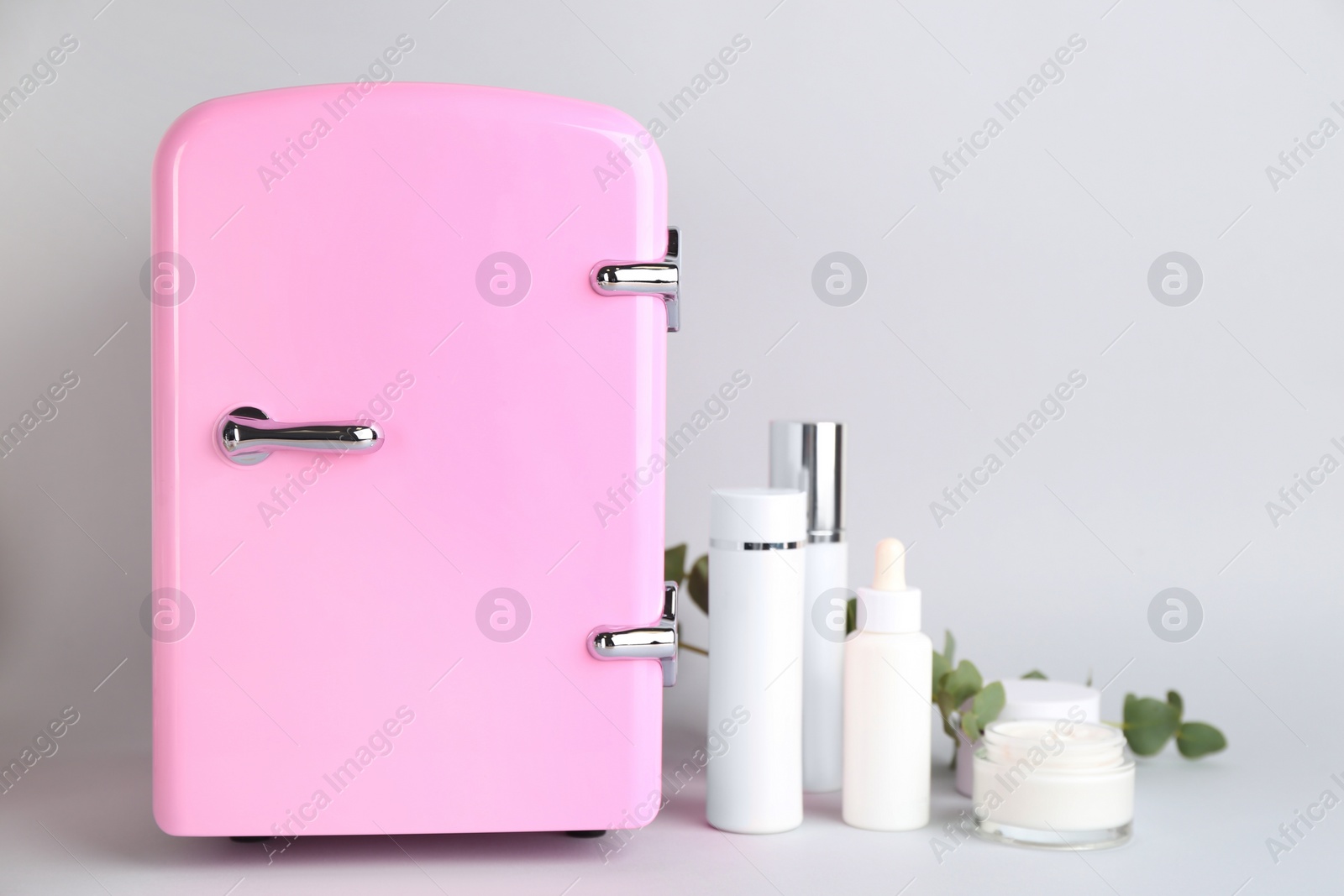 Photo of Cosmetic refrigerator and skin care products on light background