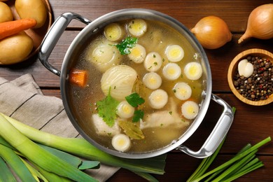 Photo of Pot with tasty bouillon and different ingredients on wooden table, flat lay