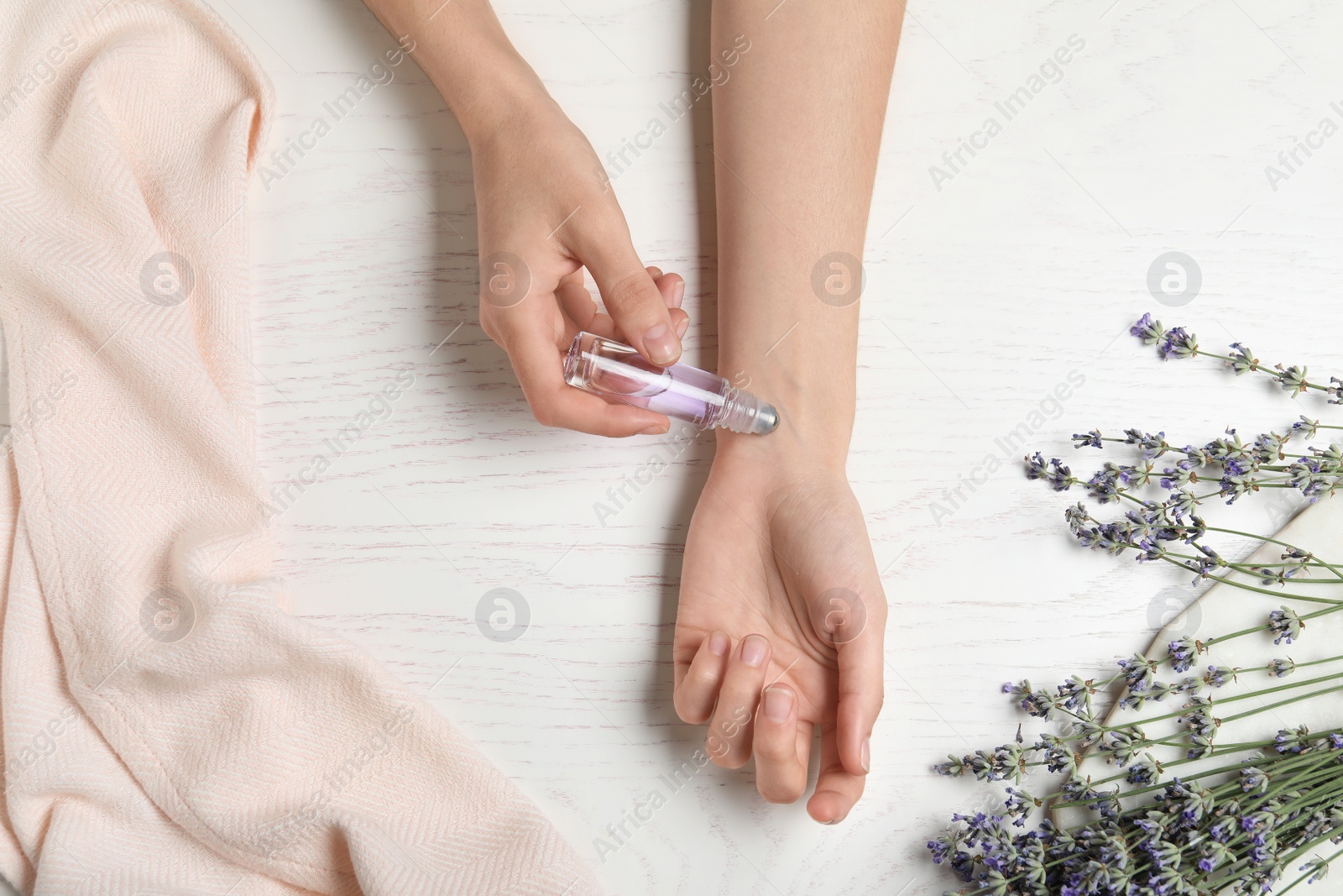 Photo of Top view of woman applying lavender essential oil at white wooden table, closeup