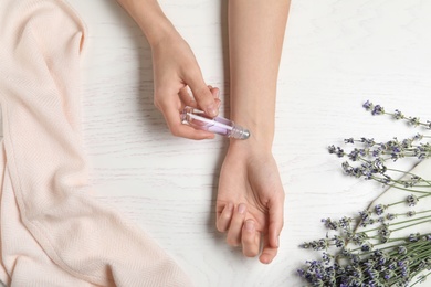 Photo of Top view of woman applying lavender essential oil at white wooden table, closeup