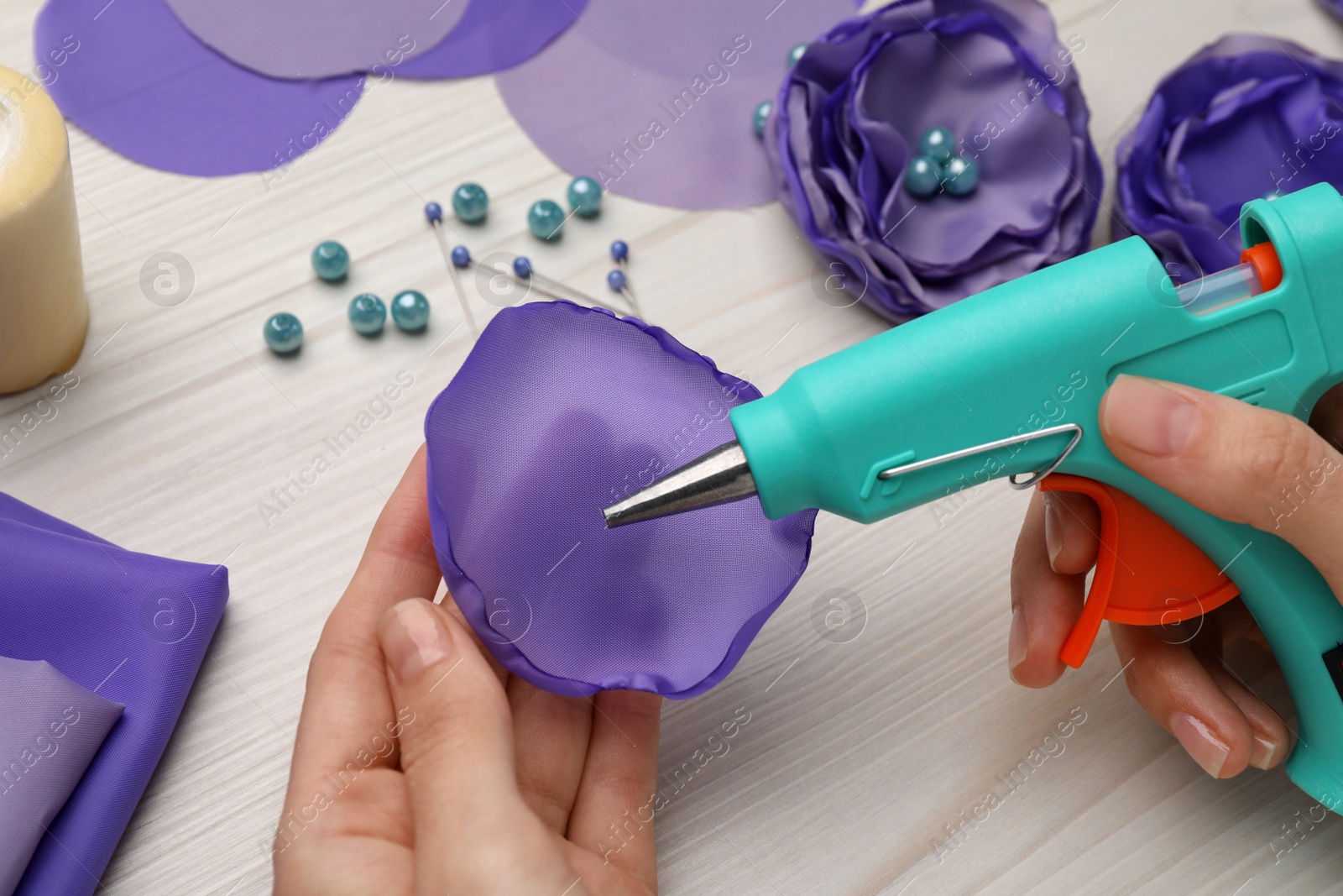 Photo of Woman with hot glue gun making craft at wooden table, closeup