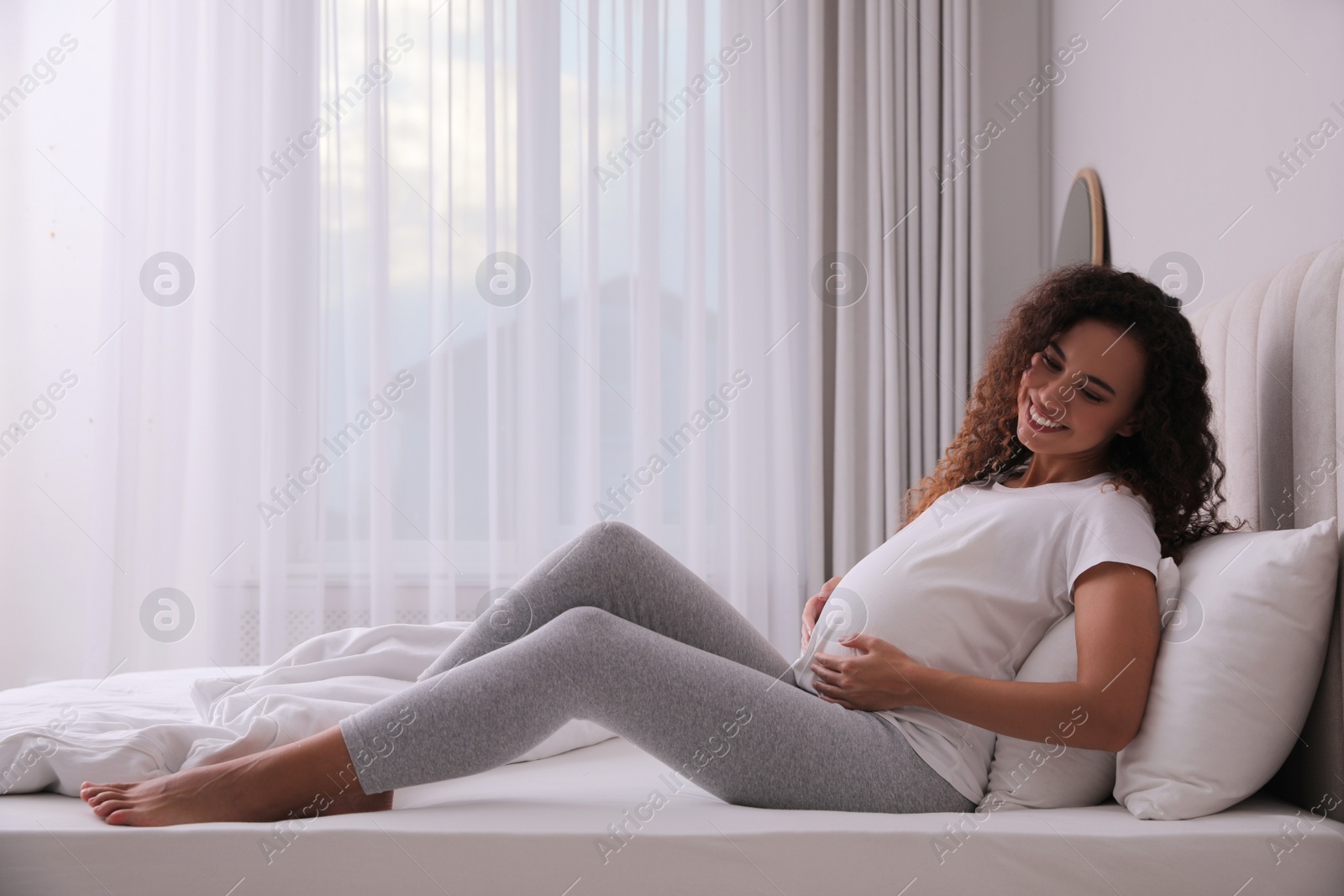 Photo of Pregnant young African-American woman sitting on bed at home