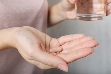 Photo of Woman holding gelatin capsule and glass of water on grey background, closeup