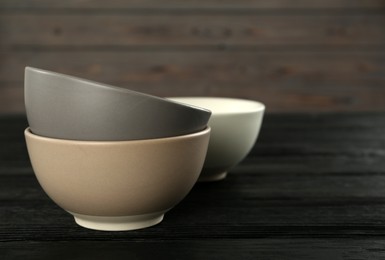 Stylish empty ceramic bowls on black wooden table, space for text. Cooking utensils