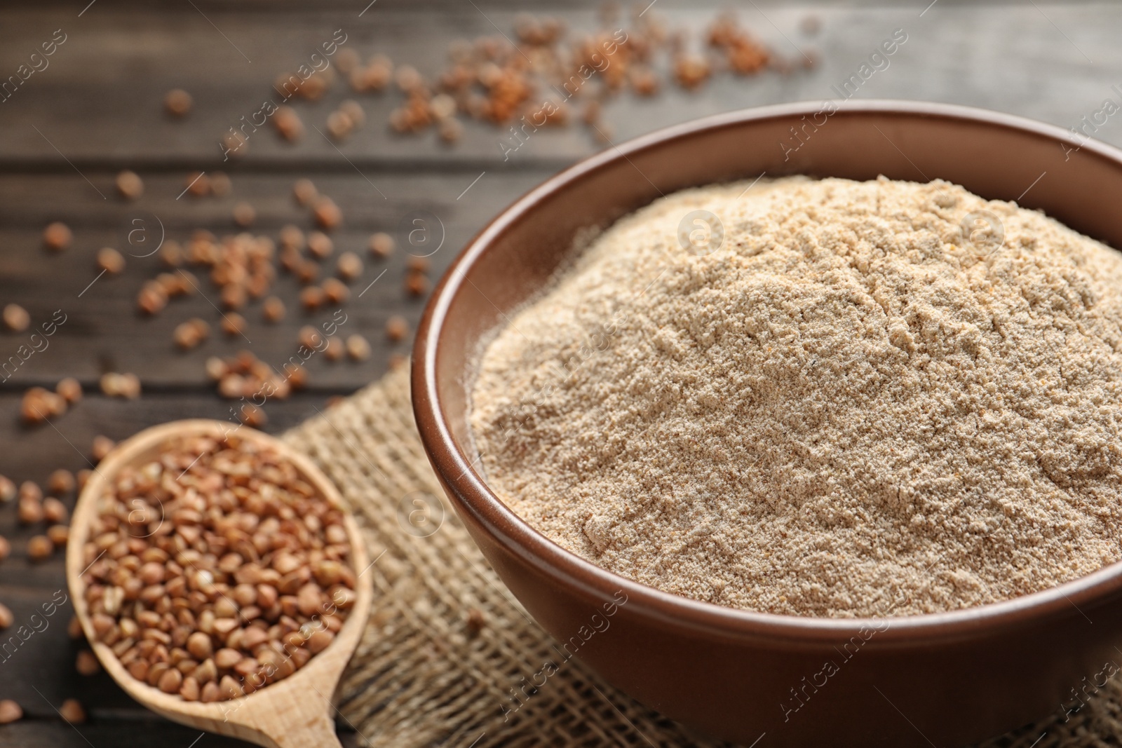 Image of Buckwheat flour in wooden bowl and spoon with seeds on table, closeup