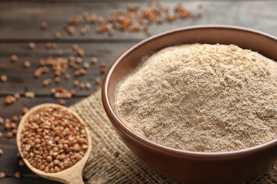 Image of Buckwheat flour in wooden bowl and spoon with seeds on table, closeup